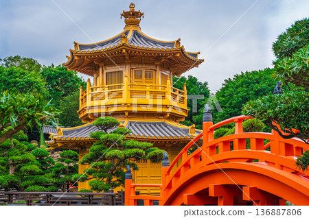 Red wooden bridge leading to Golden Pavilion Nan Lian Garden Hong Kong traditional Chinese architecture landmark park green trees blue sky view 136887806