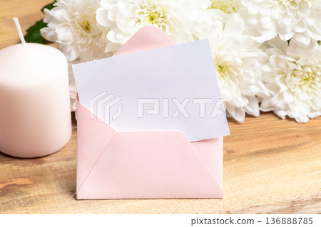 Pink envelope with blank card and white flowers on wooden table 136888785