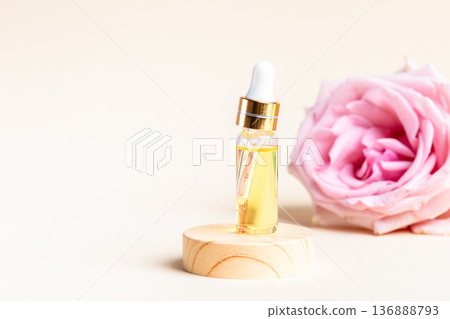 Rose essential oil dropper bottle beside pink rose on wooden base Copy space 136888793
