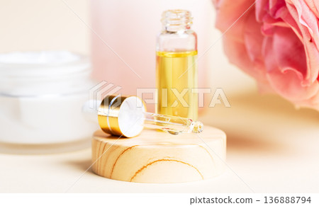 Rose essential oil bottle with dropper and cream jar on wooden stand 136888794