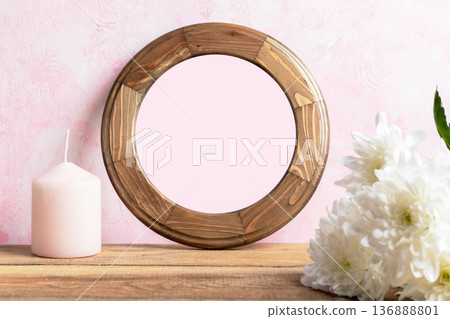 Round blank wooden frame with pink backdrop and candle and white flowers on wooden table Copy space 136888801