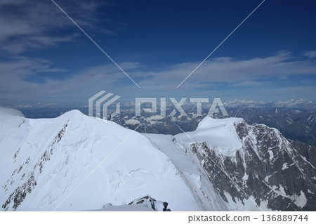 A stunning rock formation covered in snow, set against a clear blue sky with fluffy clouds in the background, creating a peaceful and breathtaking mountain landscape. 136889744