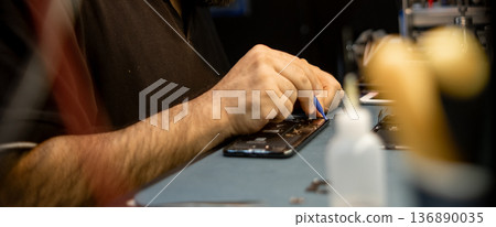 Expert Technician Repairs Smartphone With Precision in a Bustling Workshop During the Day 136890035