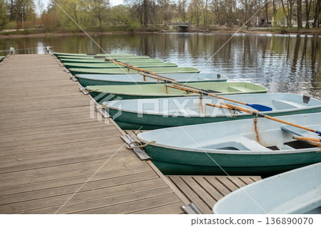 Rowboats Lined on Wooden Dock at Peaceful Lake Surrounded by Trees in Springtime 136890070