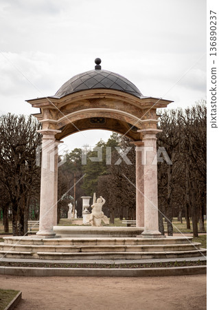 Elegant Garden Pavilion Surrounded by Neatly Trimmed Trees and Classical Sculptures in a Serene Park Setting Under Soft Cloudy Skies 136890237