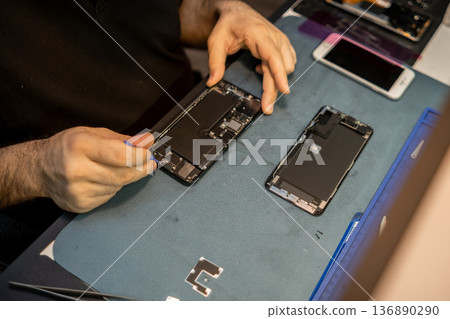 Expert Phone Technician Repairs Smartphone Components in a Dedicated Workspace, Showcasing Precision and Skill in Phone Repair on a Recent Afternoon 136890290