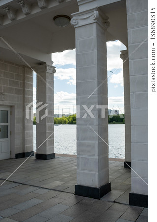 Elegant Architectural Structure Near Water Featuring Tall Columns and Scenic Views Under a Bright Blue Sky With Clouds and Greenery in the Background Elegant Architectural Structure Near Water Featuring Tall Columns and Scenic Views Under a Bright Blue Sky With Clouds and Greenery in the Background 136890315