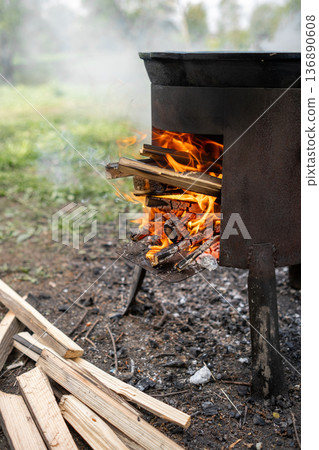 Wood Fire Cooking Pot Heating Over an Outdoor Flame With Stacked Firewood Nearby Wood Fire Cooking Pot Heating Over an Outdoor Flame With Stacked Firewood Nearby 136890608