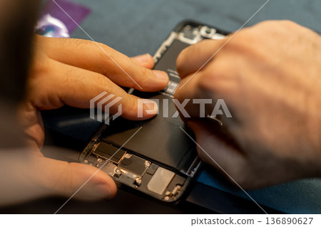 Phone Repair Technician Replacing Battery in Smartphone Inside Workshop During Daylight Hours Phone Repair Technician Replacing Battery in Smartphone Inside Workshop During Daylight Hours 136890627