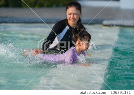mother with preschool child girl kicking water splashing by her legs while practicing swimming in edge of pool mother with preschool child girl kicking water splashing by her legs while practicing swimming in edge of pool 136891381