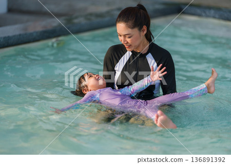 preschool child girl playing and swimming with her mother in pool 136891392