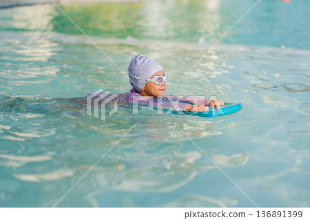 preschool child girl learning to swim with board in swimming pool preschool child girl learning to swim with board in swimming pool 136891399