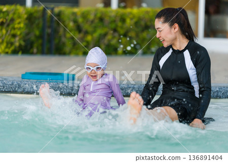 mother with preschool child girl kicking water splashing by legs while practicing swimming in edge of a pool 136891404