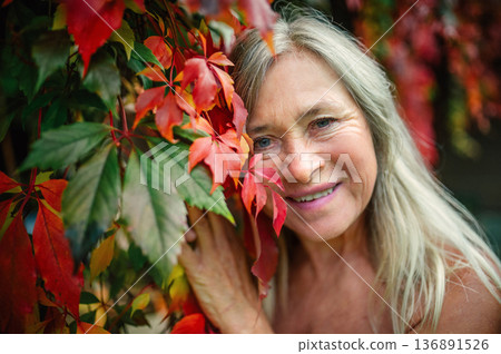 Happy elderly woman sitting in autumn foliage. Happy elderly woman sitting in autumn foliage. 136891526