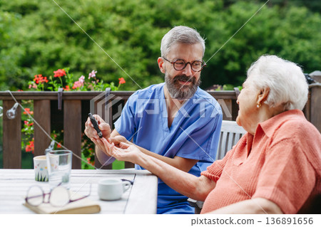 Nurse helping elderly woman measure blood sugar with glucometer. Nurse helping elderly woman measure blood sugar with glucometer. 136891656