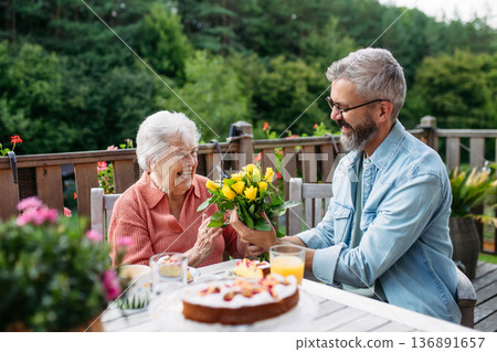 Portrait of mature son bringing bringing flowers to old mother. Portrait of mature son bringing bringing flowers to old mother. 136891657