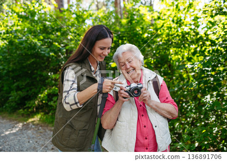 Elderly mother and daughter admire wildlife during forest walk. 136891706