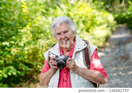 Elderly woman photographing nature during forest walk. Elderly woman photographing nature during forest walk. 136891707