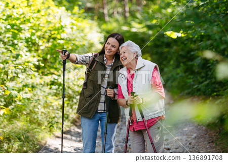 Senior woman and daughter enjoying hike with trekking poles. 136891708