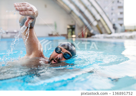 Focused swimmer performing crawl stroke in water. 136891752