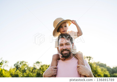 Dad carrying little boy on shoulders during warm summer day. Dad carrying little boy on shoulders during warm summer day. 136891789