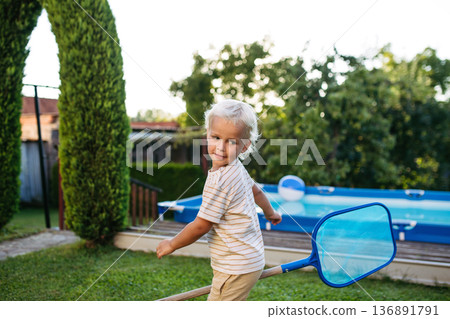 Smiling blond child playing in garden during warm summer day. Smiling blond child playing in garden during warm summer day. 136891791