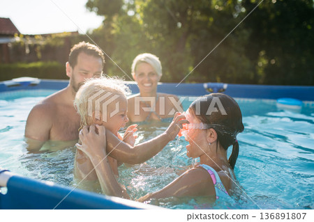 Young family with two children in swimming pool outdoors in backyard garden. 136891807