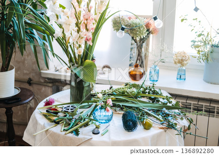 Floral arrangements and various tools sit on table in bright studio. Floral design techniques, flower pruning, professional florist tools, arrangement mechanics. Floral arrangements and various tools sit on table in bright studio. Floral design techniques, flower pruning, professional florist tools, arrangement mechanics. 136892280
