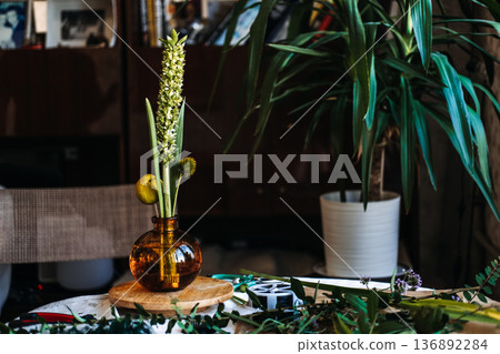Hands arrange botanical elements in amber glass vase on wooden base. Botanical art therapy, hands-on wellness, reducing anxiety through craft. 136892284