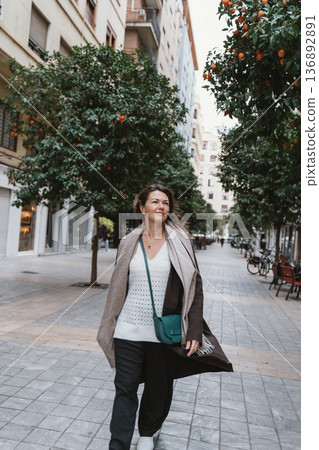 Woman Walking Confidently on City Street Lined with Orange Trees Woman Walking Confidently on City Street Lined with Orange Trees 136892891