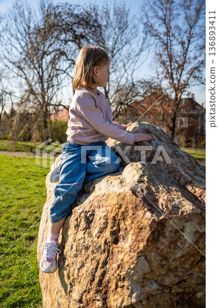 Little girl jumping on decorative stones in city park. Active spring play and outdoor childhood lifestyle. 136893411