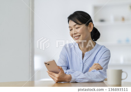 一位年近六十、面帶微笑的女士正在看著她的智慧型手機螢幕。 136893511