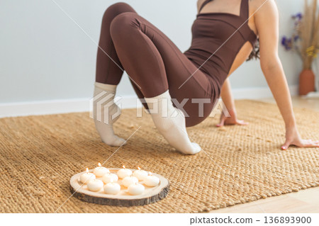 Young woman practicing yoga strength pose indoors. Balance and core training on natural mat, candles nearby, minimal calm interior, wellness, mindfulness and healthy lifestyle concept. Young woman practicing yoga strength pose indoors. Balance and core training on natural mat, candles nearby, minimal calm interior, wellness, mindfulness and healthy lifestyle concept. 136893900