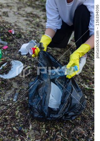 Volunteer collecting plastic waste during beach cleanup, removing litter and protecting the shoreline environment. Volunteer collecting plastic waste during beach cleanup, removing litter and protecting the shoreline environment. 136894096