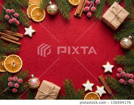 Christmas flat lay background on red felt with frame of pine branches, gifts, dried oranges, cinnamon sticks, and cookies 136894176