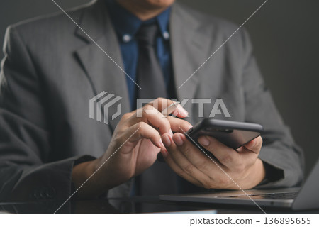 Close-up hand businessman holding smartphone pen. Working office desk. Modern business technology, mobile connectivity, online networking, professional communication, check project data. Close-up hand businessman holding smartphone pen. Working office desk. Modern business technology, mobile connectivity, online networking, professional communication, check project data. 136895655