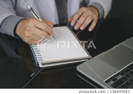 Doctor hand pen writing notes notebook. Medical healthcare concept. Physician work office desk, laptop. Write patient prescription, diagnosis, report, treatment plan. Close-up record history data. Doctor hand pen writing notes notebook. Medical healthcare concept. Physician work office desk, laptop. Write patient prescription, diagnosis, report, treatment plan. Close-up record history data. 136895663