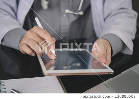 Medical doctor using tablet for telemedicine consultation online. Digital healthcare technology for virtual patient diagnosis. Physician working in clinic with modern health service and application. 136896502