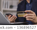 Man hand holding credit card, using smartphone for online shopping payment. Businessman making e-commerce transaction, purchasing on internet with laptop. Digital banking and secure payment concept. 136896527