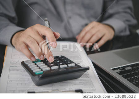 Man hand using calculator for financial analysis, tax calculation. Businessman working on accounting report with document, laptop on office desk. Business finance, budgeting concept. 136896528