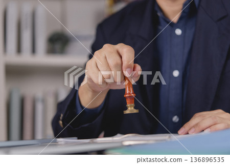 Notary public or lawyer hand with vintage brass seal stamp over document. Authenticating will, testament, or legal paperwork. Symbol of trust, legacy, and official certification. Notary public or lawyer hand with vintage brass seal stamp over document. Authenticating will, testament, or legal paperwork. Symbol of trust, legacy, and official certification. 136896535