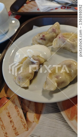 Boiled dumpling with sour cream served on white plate with cup of tea in cafe. Concept of traditional cuisine, comfort food and homemade meal 136898092