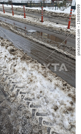 Dirty snow and slush on urban road with puddle and traffic bollard in winter day. Concept of seasonal weather, city infrastructure and hazardous driving condition 136898099