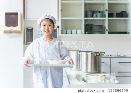 一名身穿白大褂、手持午餐盤的學校午餐值班女孩 一名身穿白大褂、手持午餐盤的學校午餐值班女孩 136899299