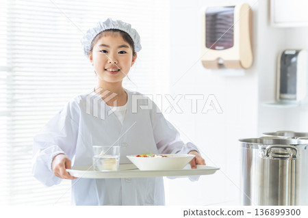 A girl on school lunch duty wearing a white coat and holding a lunch plate A girl on school lunch duty wearing a white coat and holding a lunch plate 136899300