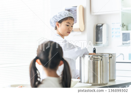 A girl on school lunch duty wearing a white lab coat and serving food from a large pot A girl on school lunch duty wearing a white lab coat and serving food from a large pot 136899302