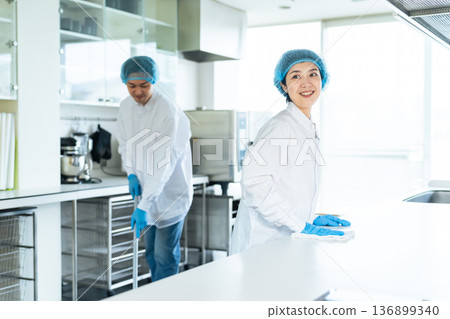 Male and female staff wearing sanitary white coats cleaning the kitchen Male and female staff wearing sanitary white coats cleaning the kitchen 136899340