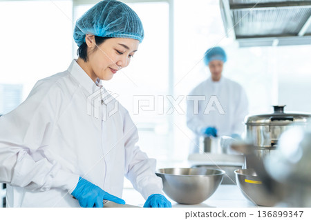 A female chef wearing a sanitary white coat cooking in the kitchen, school lunch center, cafeteria A female chef wearing a sanitary white coat cooking in the kitchen, school lunch center, cafeteria 136899347
