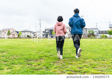 Back view of a couple running on the grass in a park Back view of a couple running on the grass in a park 136899373