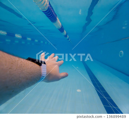 Underwater swimming pool lane with smartwatch and reaching hand 136899489
